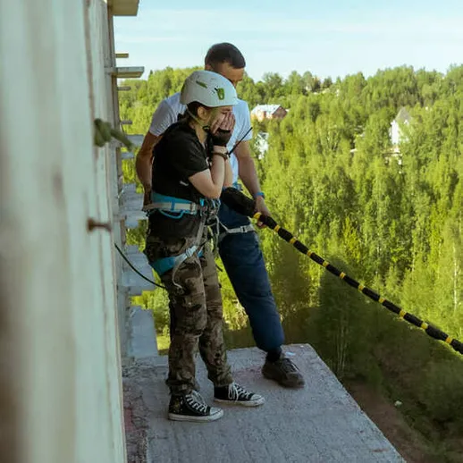 Экстремальные ощущения: девушка готовится к прыжку с высоты на фоне зеленого леса