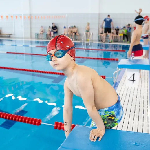 Мальчик в купальнике готовится к плаванию на соревнованиях в бассейне с синим водой и красными буйками