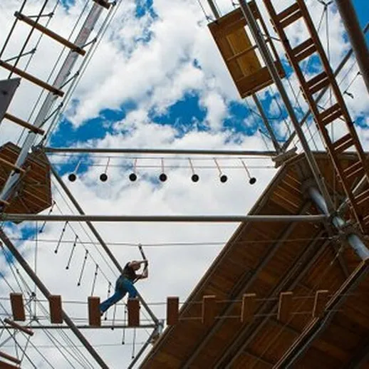 Молодой человек преодолевает веревочный курс в парке приключений под ярким небом