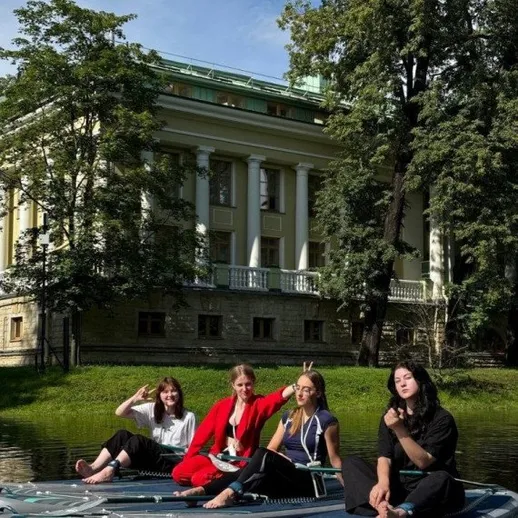 Четыре девушки наSUP-досках отдыхают у исторического здания в парке в солнечный день