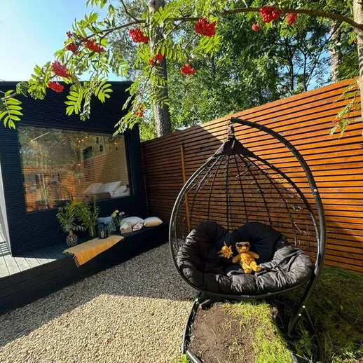 Уютный уголок в саду с коконом и мягкими игрушками на фоне стильного дома в солнечный день