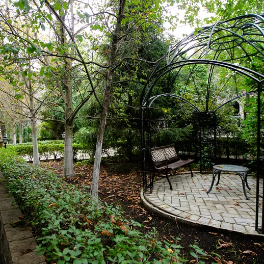 Уютная беседка в зеленом саду с извивающейся дорожкой и густыми деревьями, осень