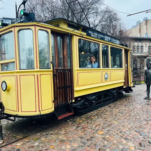 Желтый трамвай на улице старого города, женщина переходит к нему в дождливый день