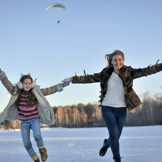 Зимние забавы на свежем воздухе: мама и дочь бегут по заснеженному озеру в солнечный день