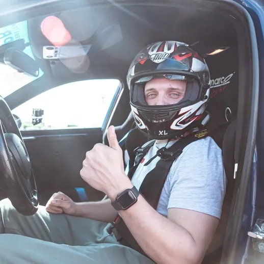 Мужчина в гоночном шлеме и сидении спортивного автомобиля показывает жест всё в порядке на трассе