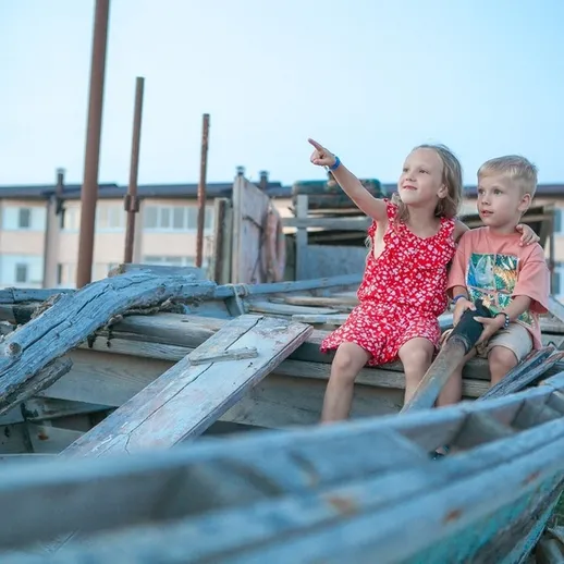 Дети на старой лодке у причала в комфортный летний день, играющие и рассматривающие окрестности