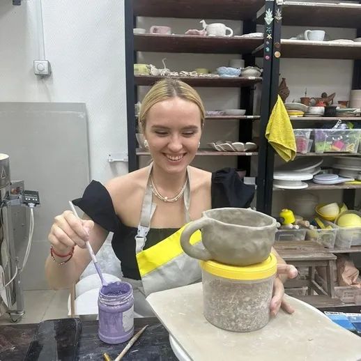 Молодая женщина занимается гончарным искусством в мастерской, создавая керамическую чашку в день с ясной погодой