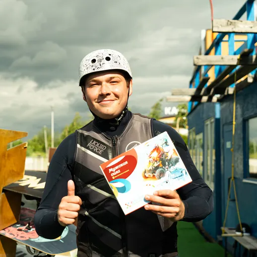 Мужчина в водной экипировке с наградой на фоне павильона для кайтсерфинга в солнечную погоду