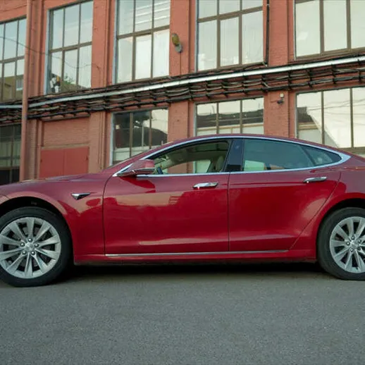 Красный электромобиль на фоне заводского здания в солнечный день, припаркованный у окон