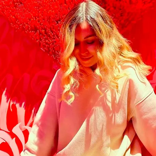 Девушка с длинными волосами в светлом худи на фоне красной стены, украшенной граффити, наслаждается моментом в солнечный день