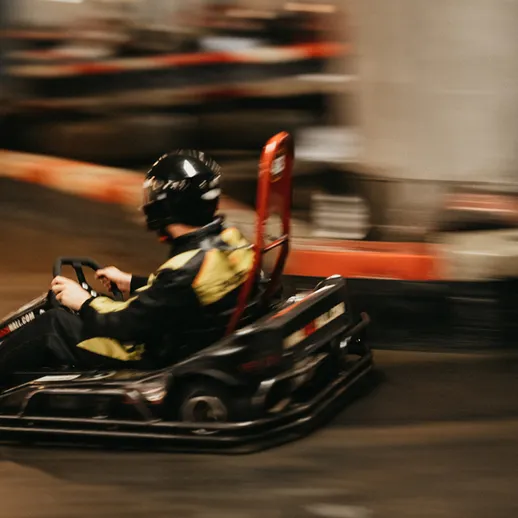 Картинг на закрытой трассе: гонщик в черной униформе мчится на поворотах в развлекательном комплексе