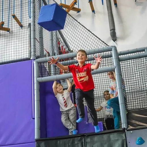 Дети в спортивном центре прыгают и ловят куб, развивая ловкость в игре на скалодроме