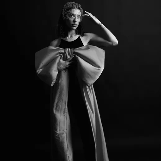 Модель в черно-белом наряде позирует на фоне темной стены, демонстрируя элегантность и стиль