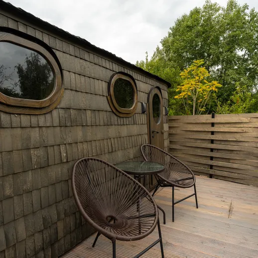 Уютная терраса с двумя стульями и столом среди зелени, расположенная рядом с деревянным домом