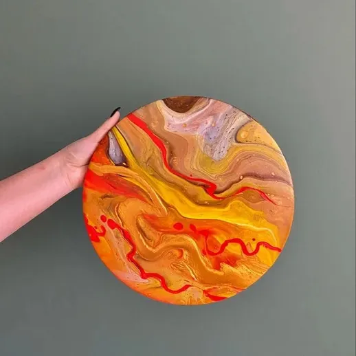 Яркая круглая искусственная тарелка с абстрактным рисунком в теплых цветах на зеленом фоне
