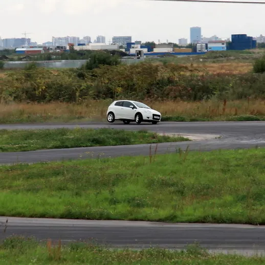 Белый автомобиль движется по извивающейся дороге на фоне городского пейзажа на рассвете