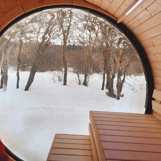 Уютная деревянная баня с круглым окном в зимнем лесу с снежным покровом