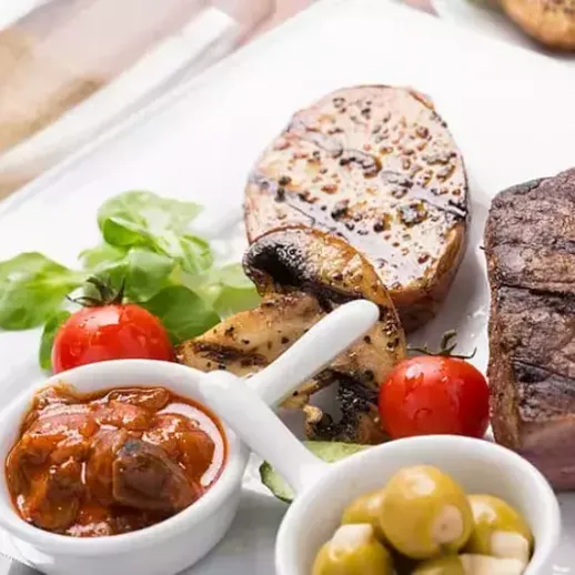 Вкусный ужин с грильованным мясом, запечёной картошкой и соусами на столе в ресторане