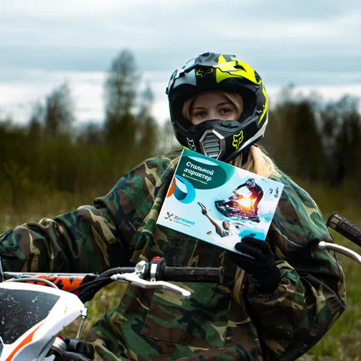 Гонщик на мотоцикле в камуфляжной одежде держит рекламный буклет на природе в пасмурный день