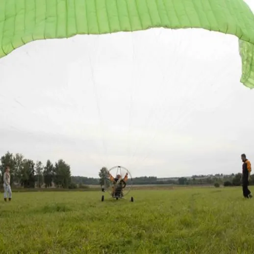 Парапланерист на поле с зелёным куполом, над ним двое наблюдателей, облачное утро в Загорске