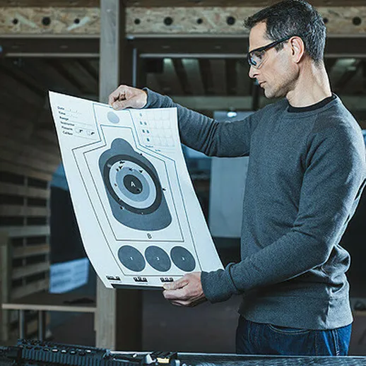 Мужчина рассматривает мишень на стрельбище в современном тире в утреннее время