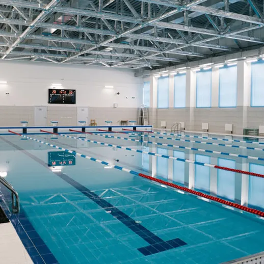 Современный бассейн с высоким потолком и чистой водой в спортивном комплексе, готовый к тренировкам в любое время суток