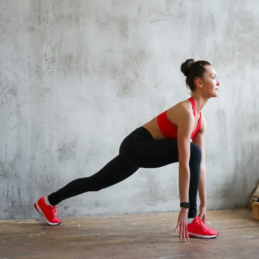 Женщина занимается растяжкой в спортивной одежде в помещении с серой стеной и деревянным полом