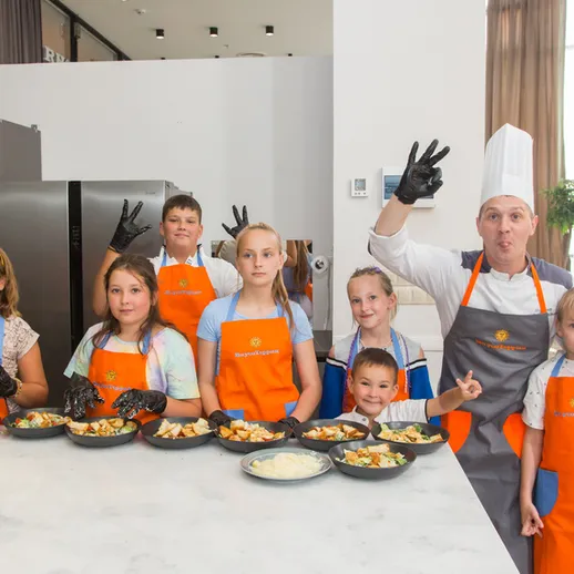 Дети готовят блюда под руководством шеф-повара в кулинарной школе во время мастер-класса