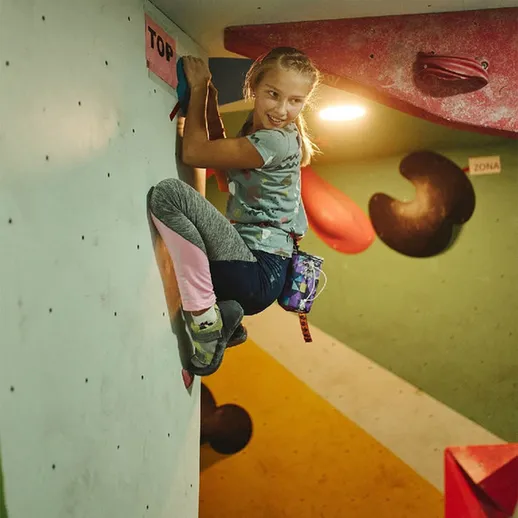 Маленькая скалолазка успешно достигает вершины скалодрома во время тренировки в спортивном центре