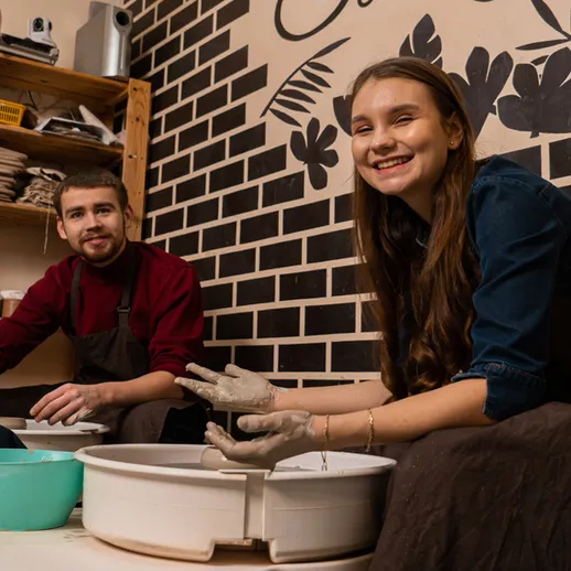 Молодая женщина и мужчина занимаются глиной в керамической студии, улыбаются на занятии в уютной атмосфере
