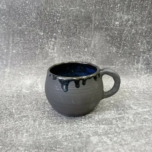 Черная керамическая чашка с каплями в интерьере на фоне текстуры