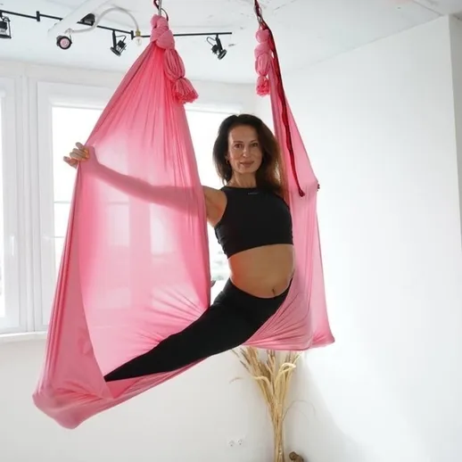 Женщина выполняет йогу на тканях в розовом гамаке в светлой комнате в течение дня