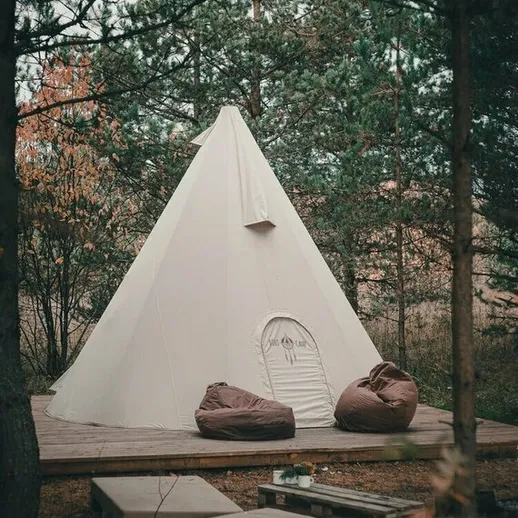Уютная белая палатка в лесу с комфортными креслами на открытой площадке