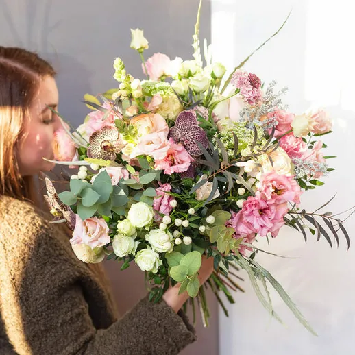 Девушка на улице улыбается, держа большой букет розовых цветов в руках в солнечный день