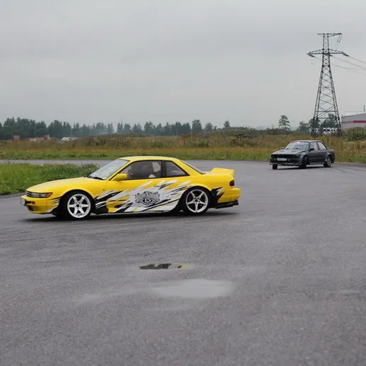 Автомобили на дрифте на закрытой трассе в серый день, природа вокруг и высокие столбы электричества