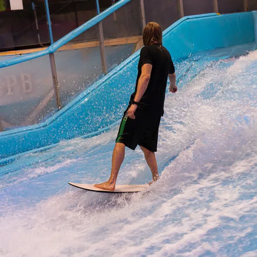 Серфингист катается на волноподобной трассе в развлекательном центре в течение дня