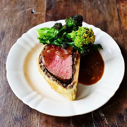 Вкусный ростбиф в тесте с зелеными овощами и соусом на белой тарелке