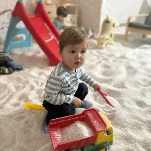 Мальчик играет с игрушечным грузовиком в песочнице в детской комнате во время зимних каникул