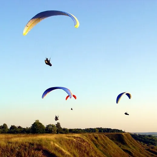 Парапланеры летают высоко над холмами в ясный день, наслаждаясь захватывающими видами на природе