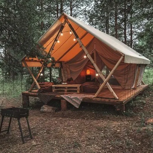 Уютный палаточный домик в лесу с огнями и деревянной террасой среди деревьев
