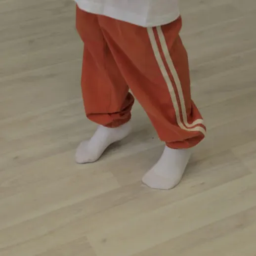 Танцующий ребенок в красных штанах и белых носках на деревянном полу в комнате