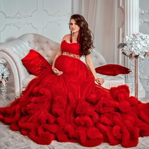 Модель в шикарном красном платье с воланами позирует в интерьере с белыми цветами и декоративными подушками