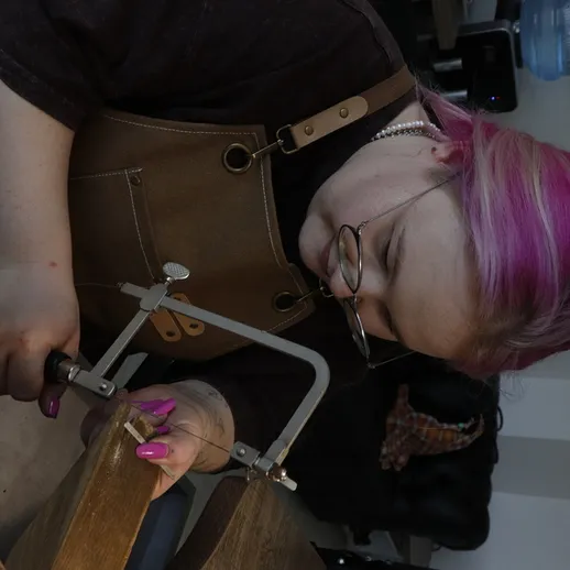 Женщина с фиолетовыми волосами работает с инструментом в мастерской, создавая уникальный предмет ручной работы