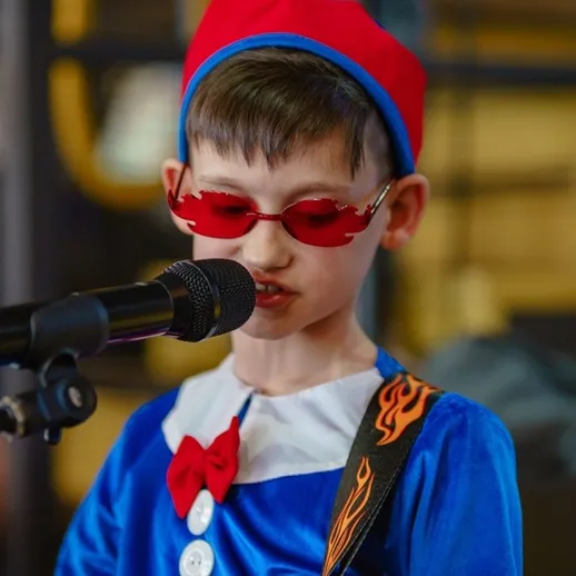Участник детского концерта исполняет песню на сцене в ярком костюме