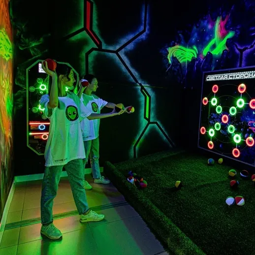 Два участника в комнате с неоновыми огнями, играют в интерактивную активность с мячами и ракетками