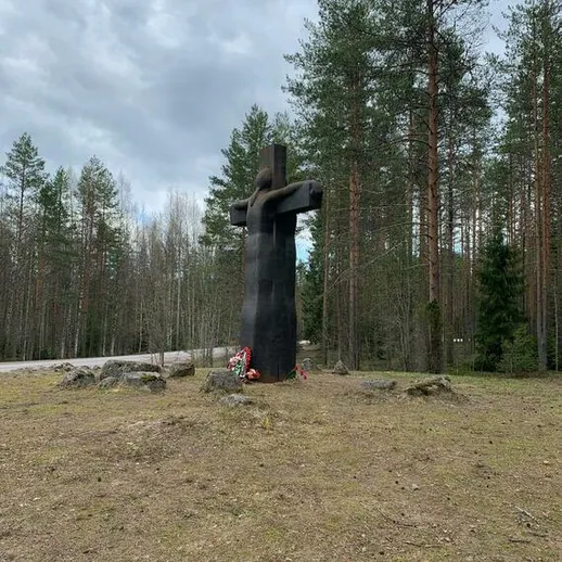 Монументальная скульптура черного креста в лесу, рядом с дорогой, в облачный день весны