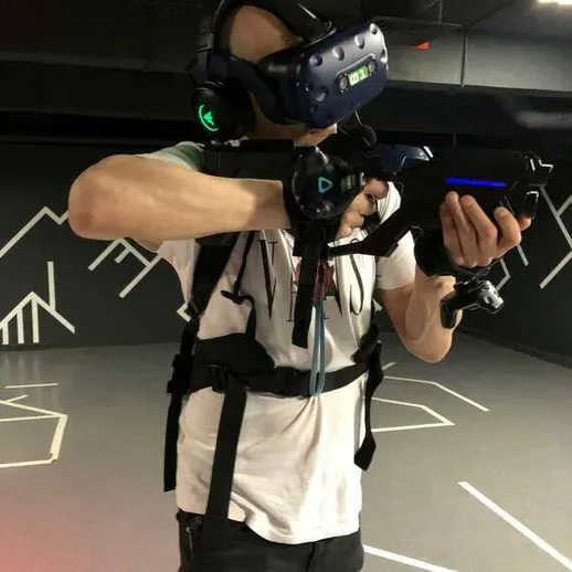 Человек в виртуальной реальности использует оружие для игры в VR-арене на фоне графики и разметки