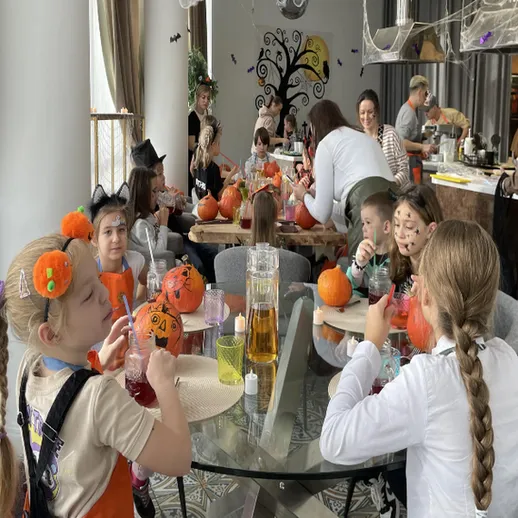 Дети участвуют в праздничном мероприятии по украшению тыкв в уютном кафе во время Хэллоуина