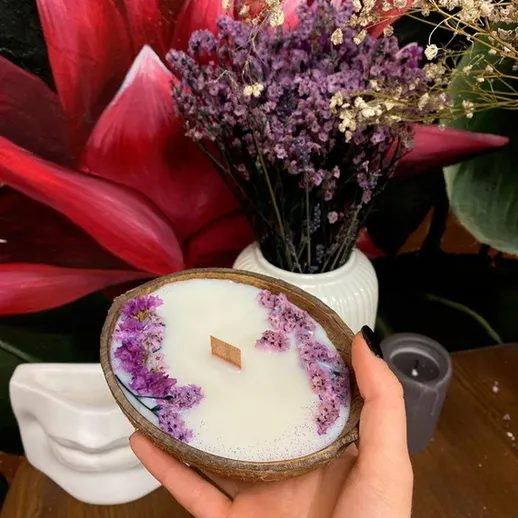 Рука держит необычную свечу с цветами в окружении стен с ярким цветочным рисунком в уютном интерьере