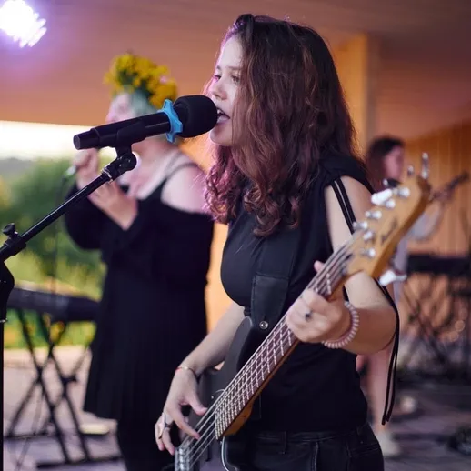 Молодая музыкантка играет на бас-гитаре во время живого выступления на открытой площадке